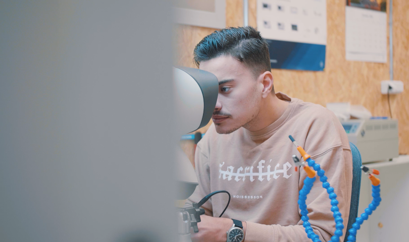 Edmir Suljic is looking into a microscope in the electronics lab